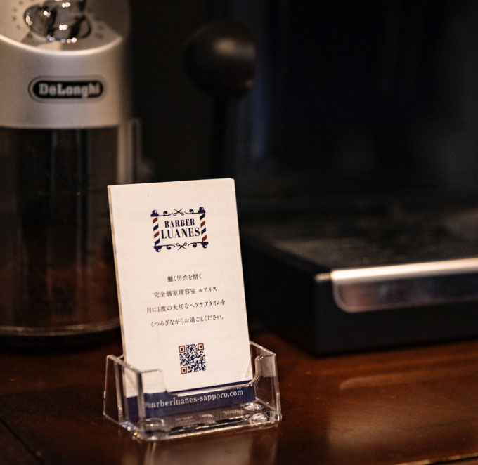 札幌の高級理容室「BARBER LUANES」の案内カードと店内のコーヒーマシン